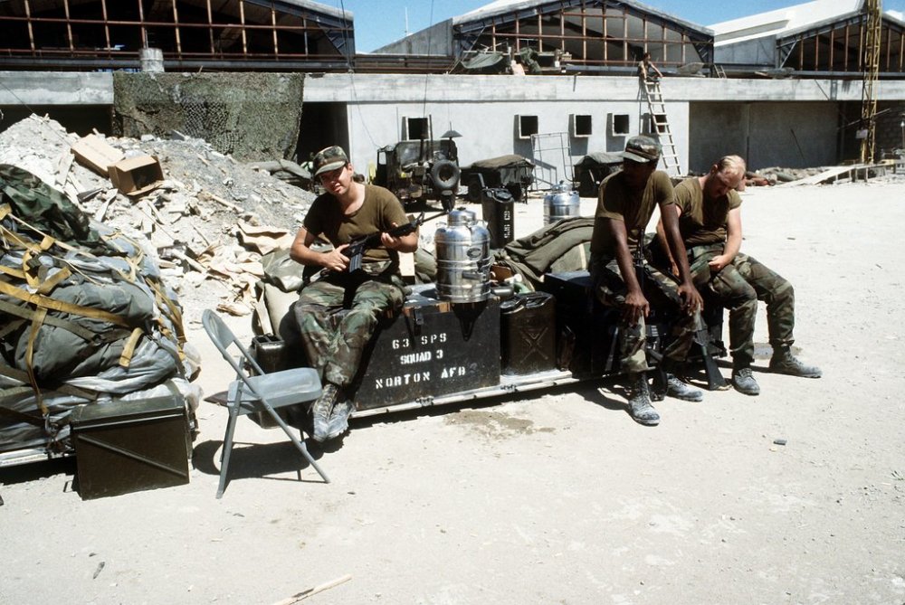Members of the 63rd Security Police Squadron sit outside the partially built terminal at Point Salines Airport during Operation Urgent Fury. One man is armed with an M-16A1 rifle.jpg